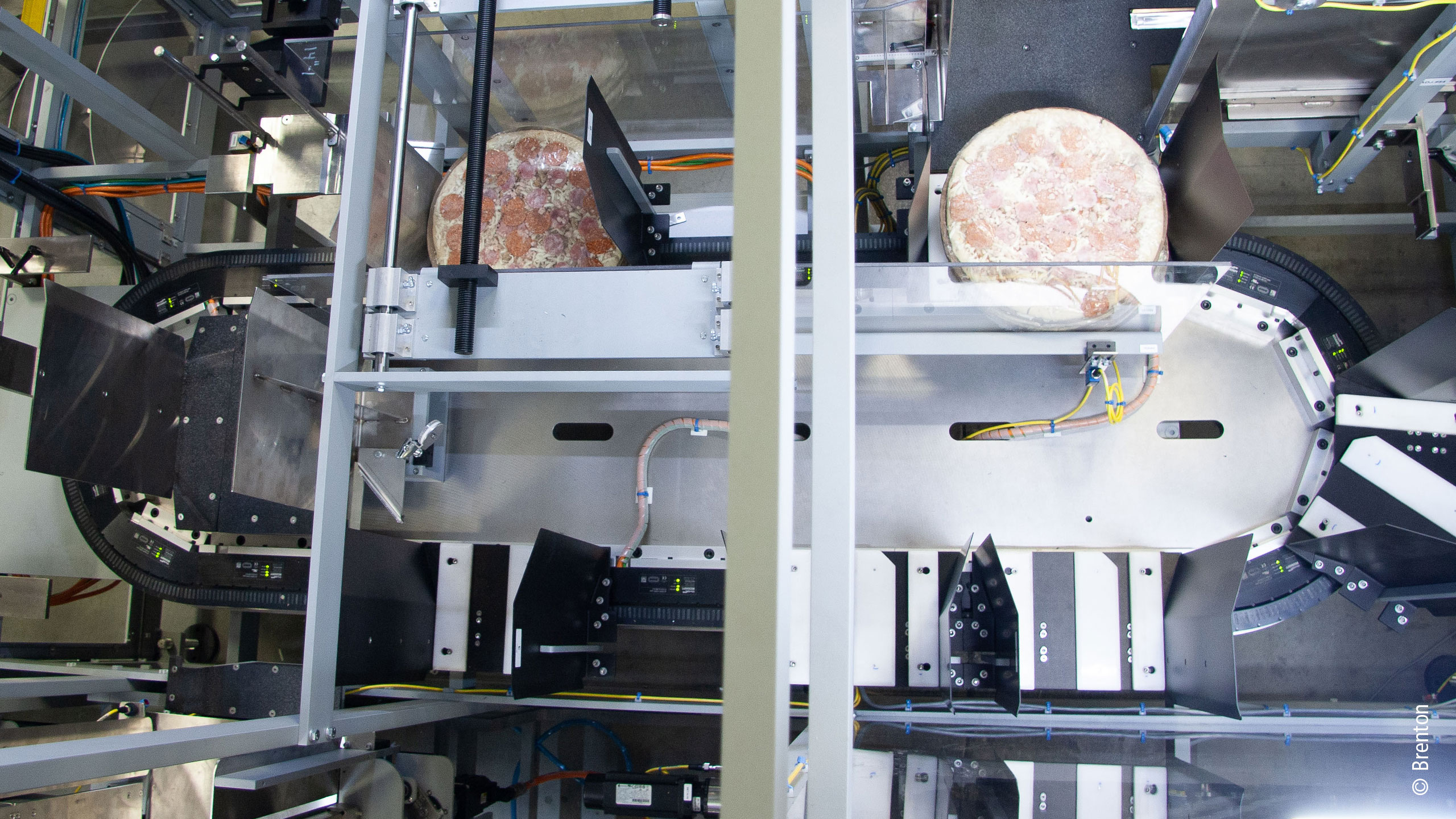 XTS 磁驱柔性输送系统是 Brenton 公司 M2000 包装机的核心，如上图：XTS 系统带着一串装有披萨的桶状物绕过 180 度的转角，抓紧并稳定披萨堆 