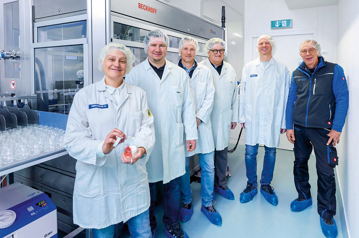 Sigrid Glanzer（Glanzer cosmetic engineering）手持一只灌装好的罐子，Gerhard Holzer 与 David Kittl（均来自倍福），Walter Steinauer 与 Hellwig Mallinger（均来自 Glanzer cosmetic engineering），以及 Christian Haslmair（Pro Pharma Automation）在灌装产线前合影（从左至右）